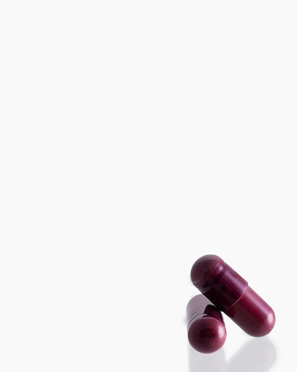 Two dark red-purple capsules lying on a clean white surface with a soft reflection below.